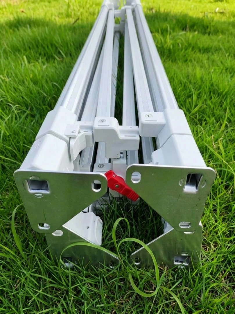 Estructura de aluminio de un gazebo plegable cerrada y compacta sobre el césped, con traba central y placas metálicas de esquina